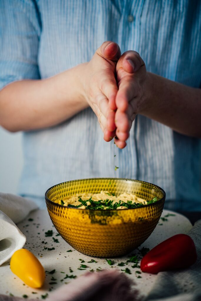 Nachhaltig vegan ernähren. Eine Person streut Petersilie über eine gelbe Schale mit Couscous.