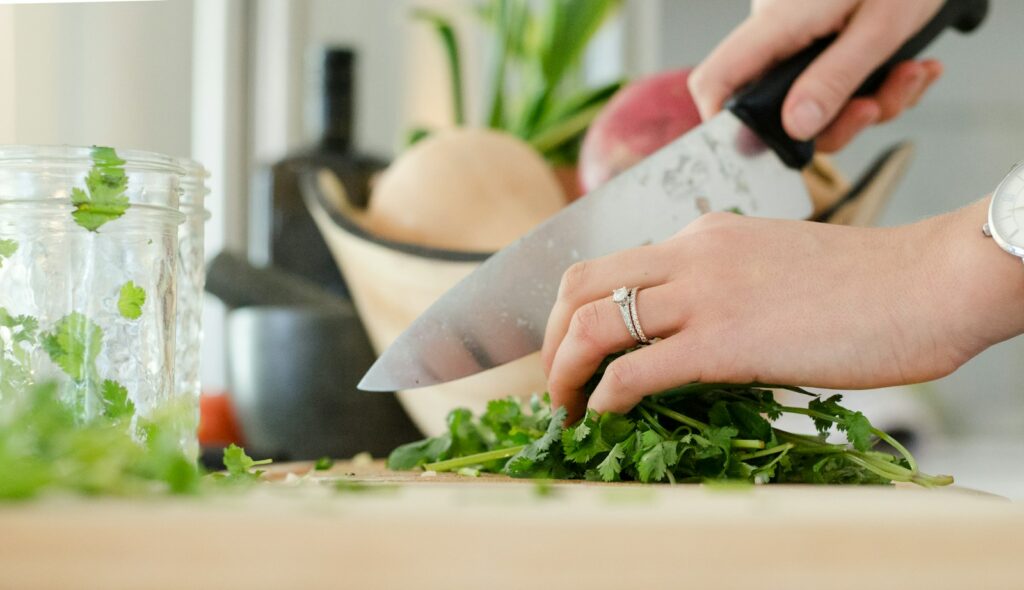 Vegan einsteigen - Hände, die Kräuter in der Küche auf einem Brett scheiden