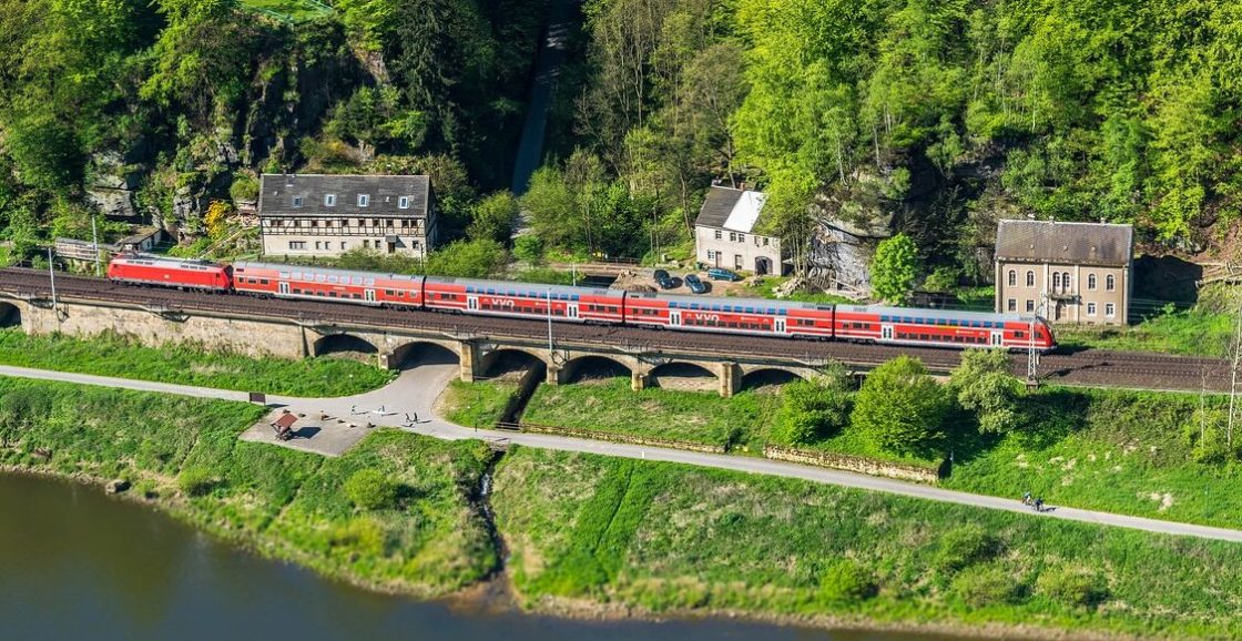 Nachhaltig reisen mit der Bahn, Zug neben der Elbe über einem Viadukt